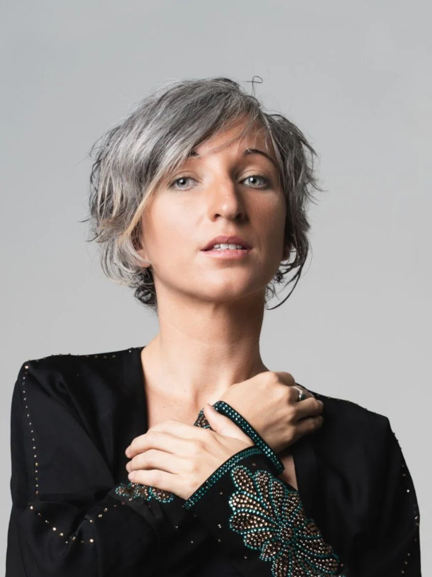 ZOE from Earth, hands crossed at her collarbone, looking into the lens